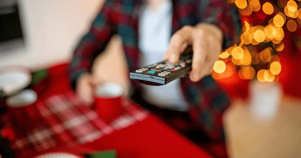 Man using remote control to watch the television whilst holding a red festive mug with Christmas tree in the background